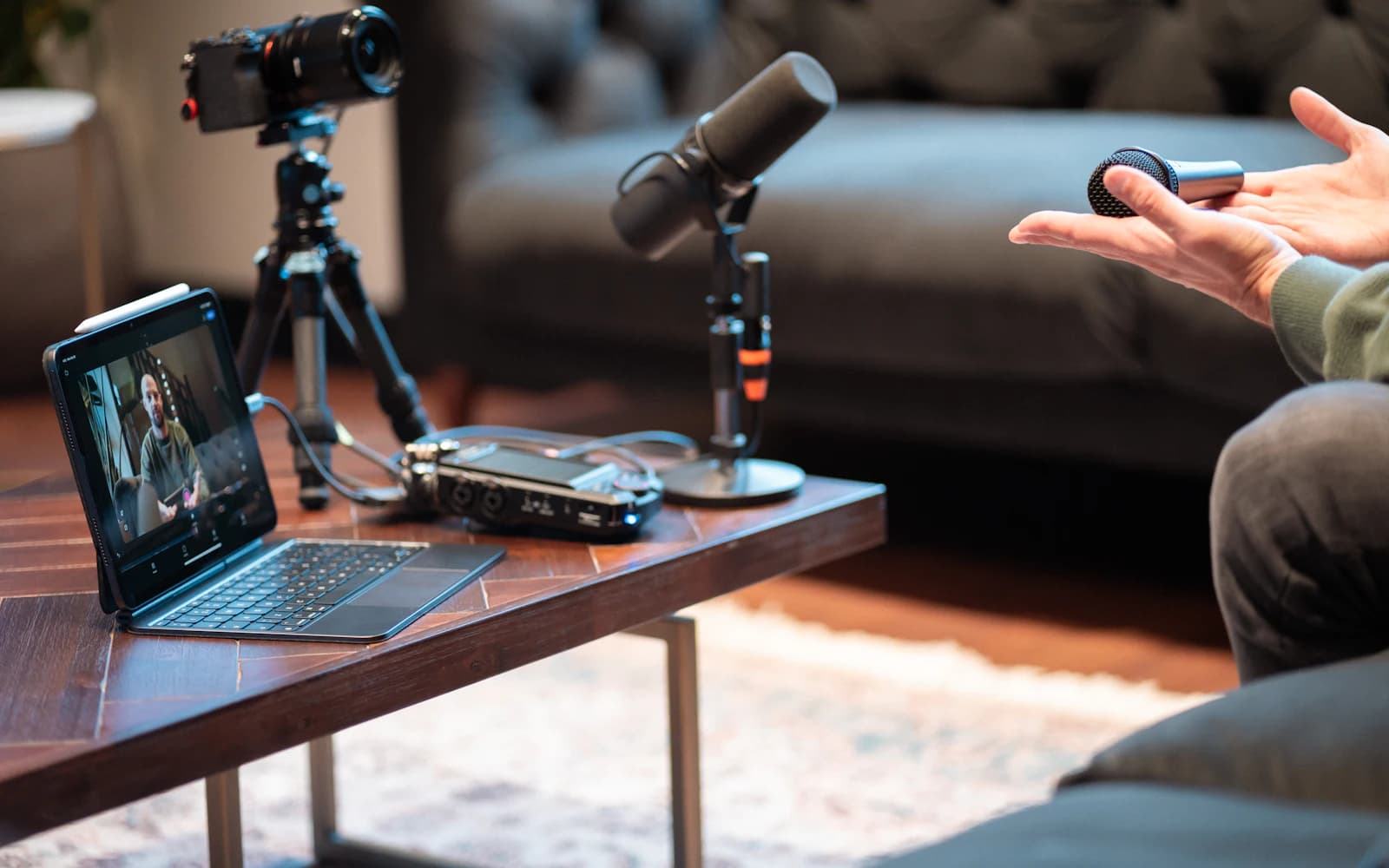 A podcast recording setup with a camera, a microphone, and a tablet on a coffee table