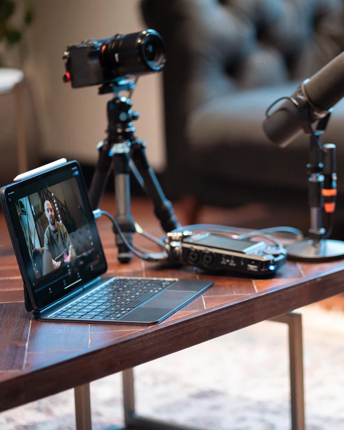 A podcast recording setup with a camera, a microphone, and a tablet on a coffee table