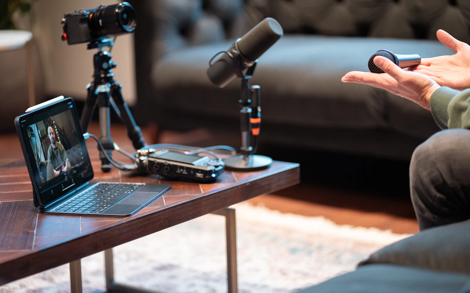 A podcast recording setup with a camera, a microphone, and a tablet on a coffee table